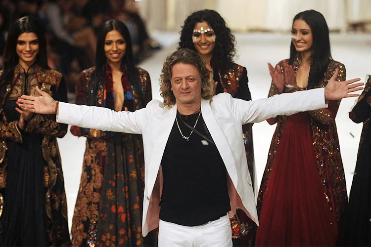 Rohit Bal standing with his arms extended at a runway finale