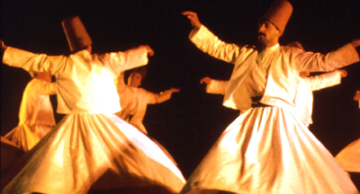 Whirling dancers in flowing cream robes under warm stage lighting