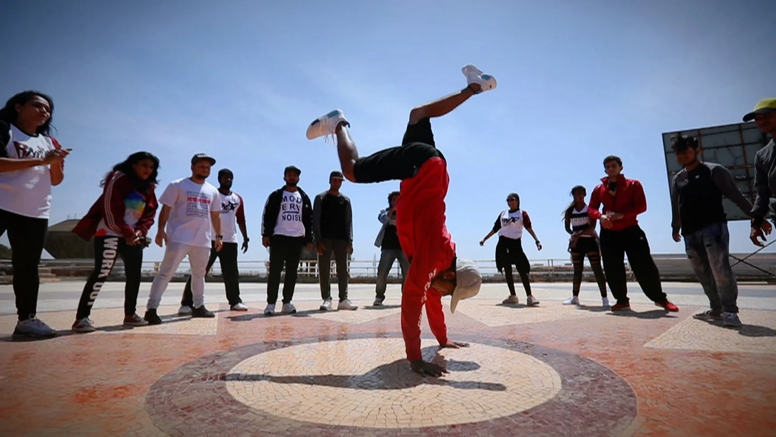 A dancer balancing on one hand as a group watches outdoors