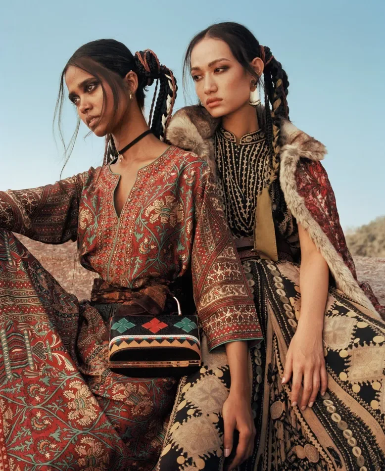 Two models wearing layered patterned garments and decorative jewelry