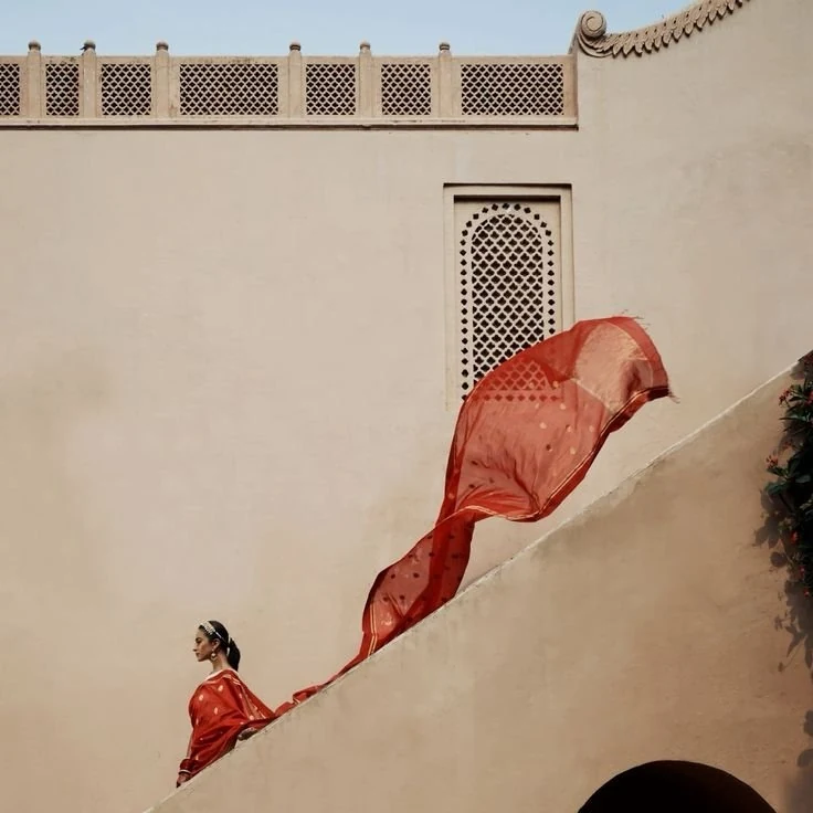 A red Chanderi saree flowing beside a palace courtyard