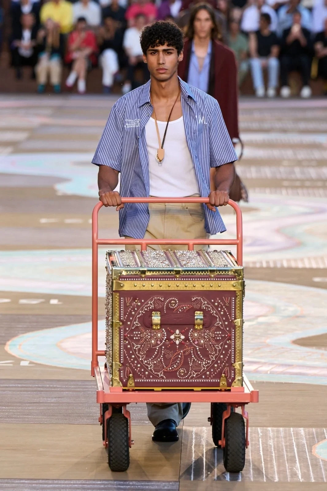 Model with a lilac shirt and a Louis Vuitton trunk on the runway